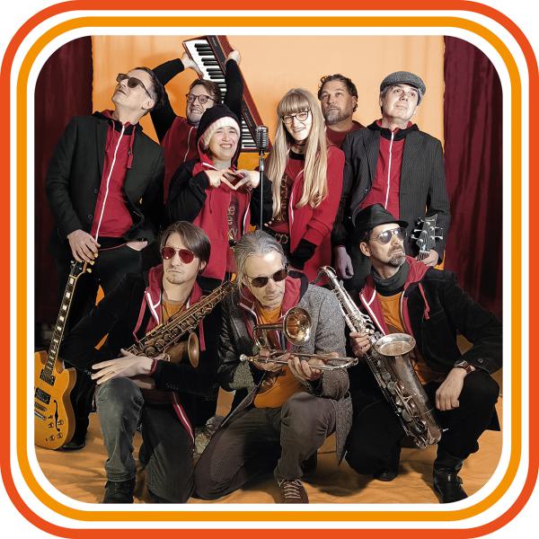 Bandfoto Hiddit: Große Bandgruppe im Studio (Gruppenfoto) Eine große Band aus mehreren Personen posiert gemeinsam in einem Innenraum vor einem farbigen Hintergrund mit grafischem Rahmen. Die Bandmitglieder stehen und knien in mehreren Reihen und halten ve